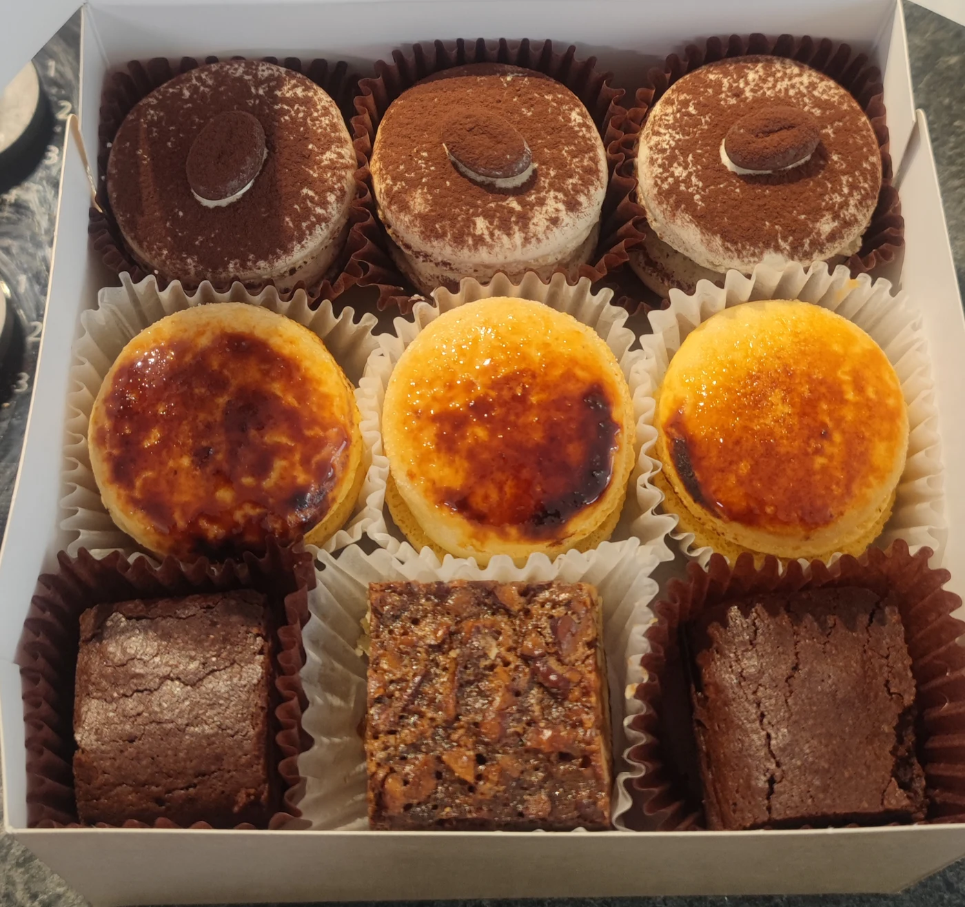 Gemengde doos met macarons, twee brownies en een pecan-pievierkantje in individuele papiertjes
